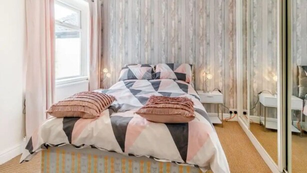 Ein Schlafzimmer mit Bett, Nachttisch, Spiegel und einem Fenster mit Vorhängen.