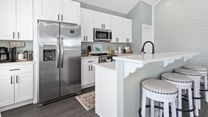Una cocina moderna con armarios blancos, electrodomésticos de acero inoxidable y una zona de bar con taburetes.