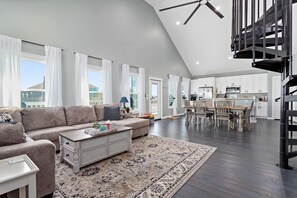 A spacious living room with a sofa, coffee table, and a patterned rug. A dining area with a table and chairs is visible in the background. - Starlink. Four Bedroom. Arcade. Fire Table. Marina. Tiki Bar. Fully Stocked. (Bolivar Peninsula)