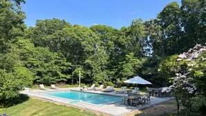 Ein Garten mit Swimmingpool, Liegestühlen und einem Tisch mit Sonnenschirmen.