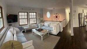 Eine moderne Küche mit Edelstahlgeräten, ein Essbereich mit roten Stühlen und ein Wohnzimmer mit großem Fenster und Wand-Fernseher.