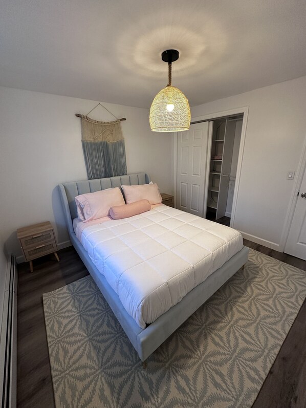 Une chambre à coucher comprenant un lit, des tables de chevet, un luminaire suspendu, une armoire et un tapis à motifs.