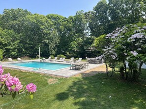 Ein Garten mit Swimmingpool, Liegestühlen und einem Esstisch.