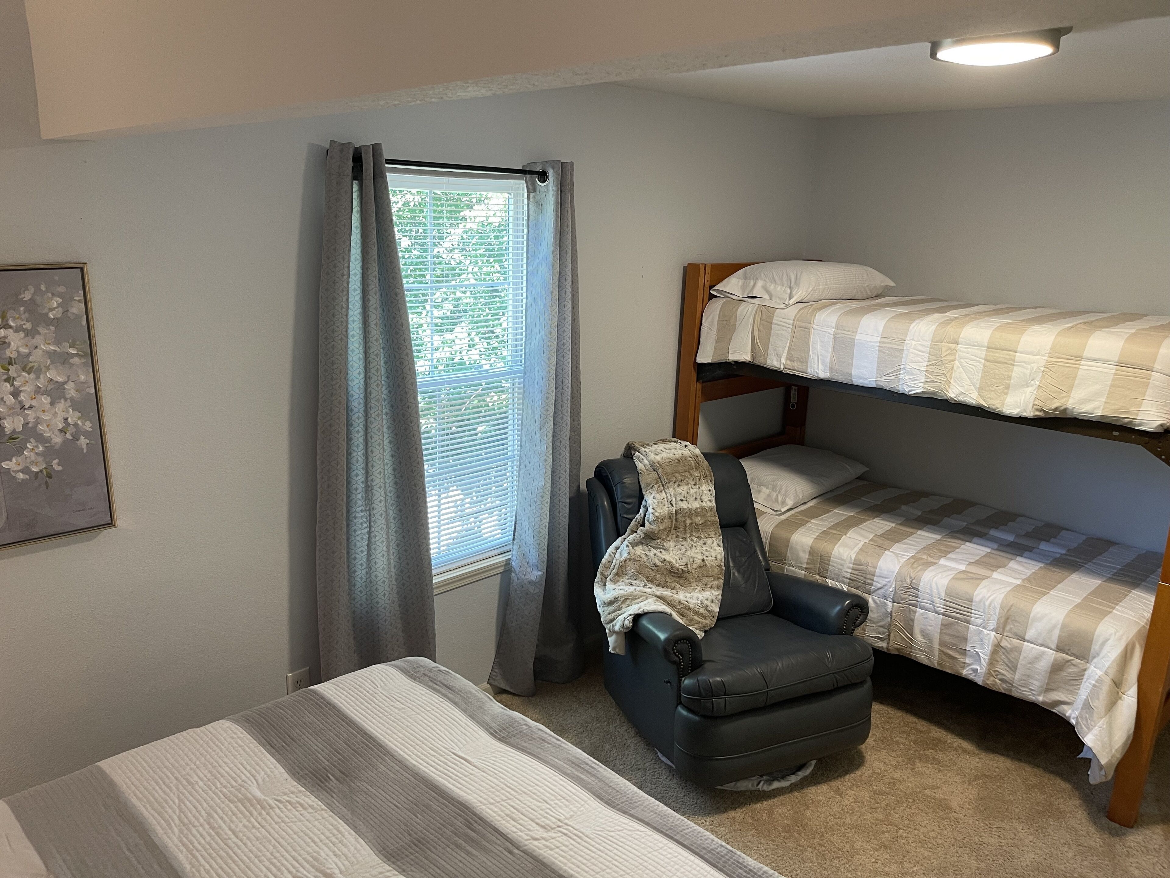Habitación pequeña con literas, una cama individual, una silla y una ventana con cortinas.