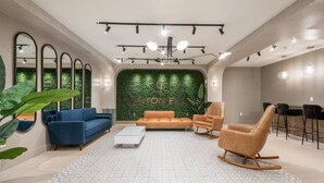 Een moderne woonkamer met een groene wand, blauwe en oranje banken, een witte salontafel en een houten schommelstoel.