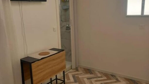 Ein Zimmer mit Fischgrätparkett, einem an der Wand montierten Flachbildfernseher, einem hölzernen Konsolentisch und einem Fenster, das für natürliches Licht sorgt.
