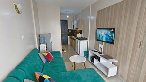 A modern living room with a green sofa, a flat-screen TV, a white coffee table, and a kitchen in the background. - Quiet Urban Stay with Views, 0742 for 616 then 120 (Nairobi)