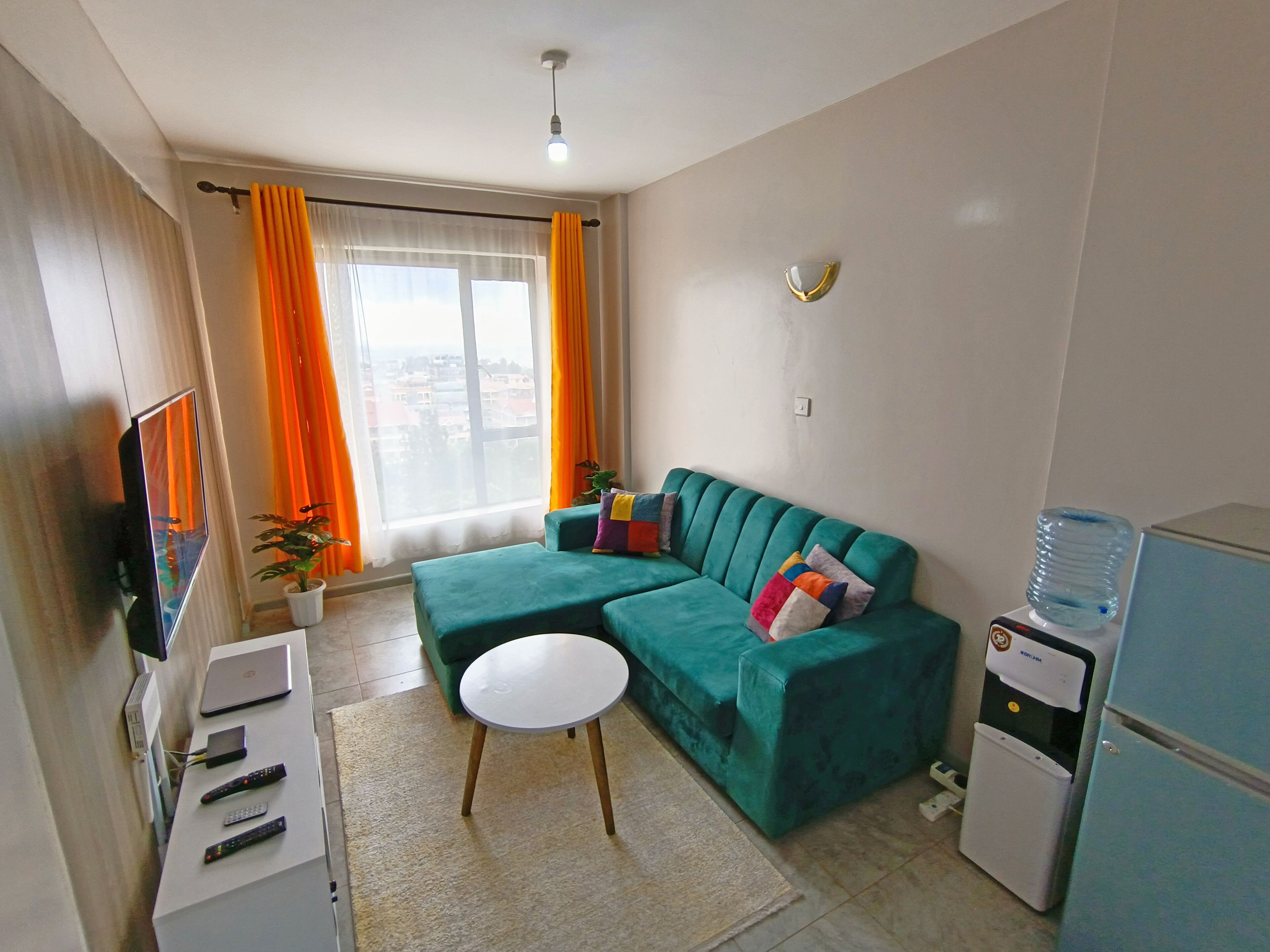 A compact living space with a sofa, a small table, a TV, and a water dispenser.