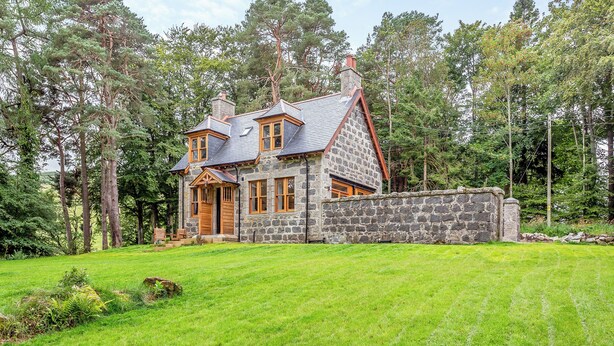 Een stenen huis met een stenen schoorsteen, houten deuren en een stenen muur.