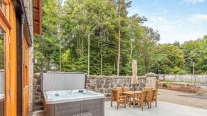 Een hottub, een houten terras, een buitentafel met stoelen en een stenen muur.