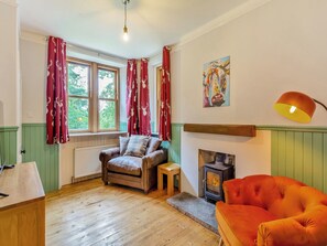A cozy room with a fireplace, a wooden floor, a leather armchair, and a red sofa.