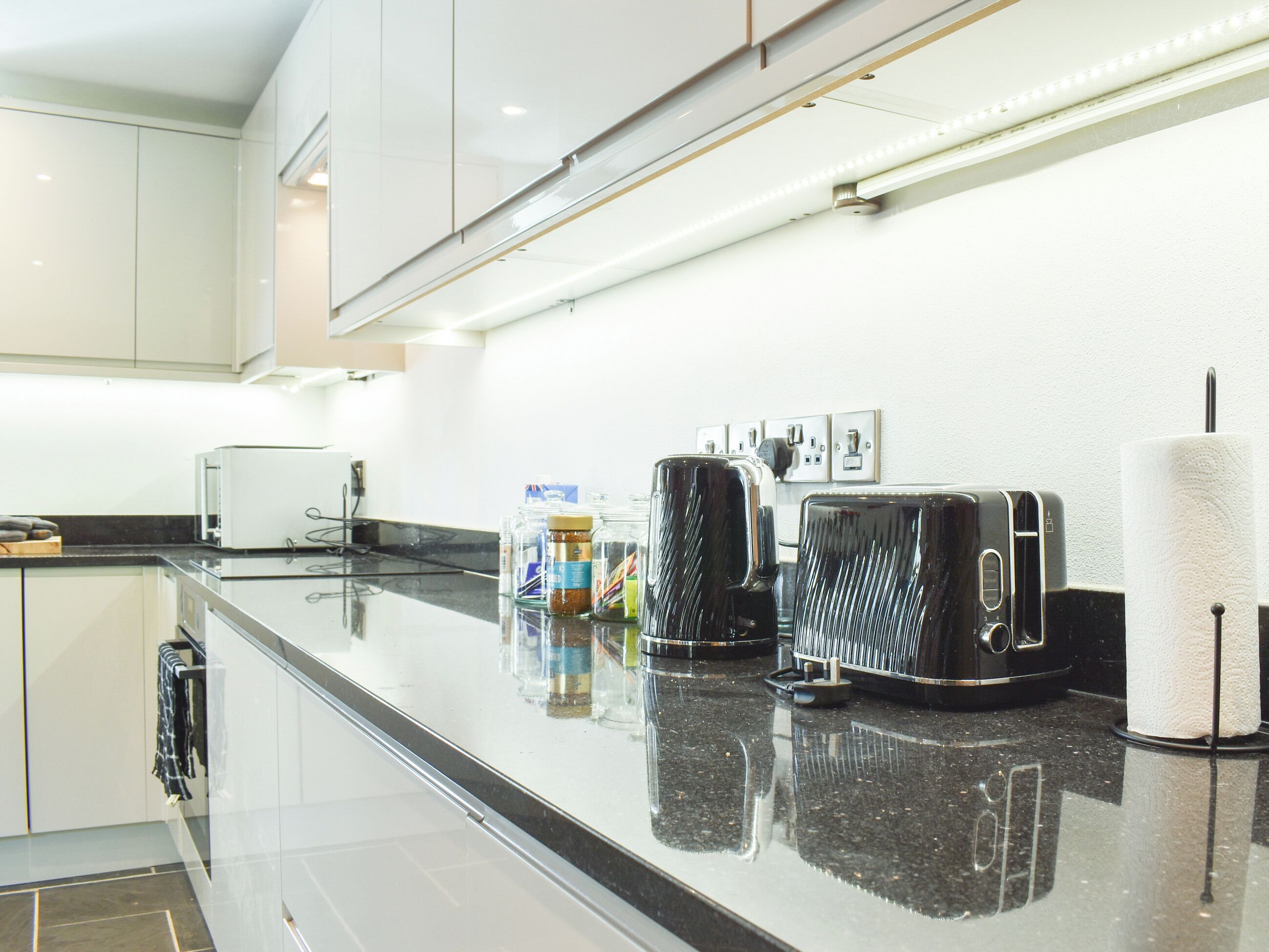 A modern kitchen with a black countertop, stainless steel appliances, and a white backsplash.