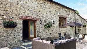 A stone building with a patio area featuring wicker furniture and a table. - Slade Barn - UK42977 (Brayford)
