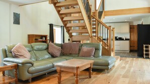 A spacious living area with a green leather sofa, a wooden coffee table, and a wooden staircase. - Slade Barn - UK42977 (Brayford)