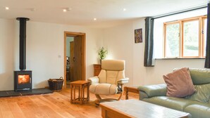 A cozy living room with a wood-burning stove, a leather sofa, a wooden coffee table, and a window with curtains. - Slade Barn - UK42977 (Brayford)