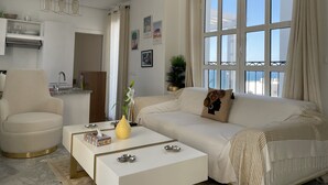 A modern living room with a sofa, a coffee table, and a dining area with a kitchen in the background. - La Perle à Marsa Plage (La Marsa)