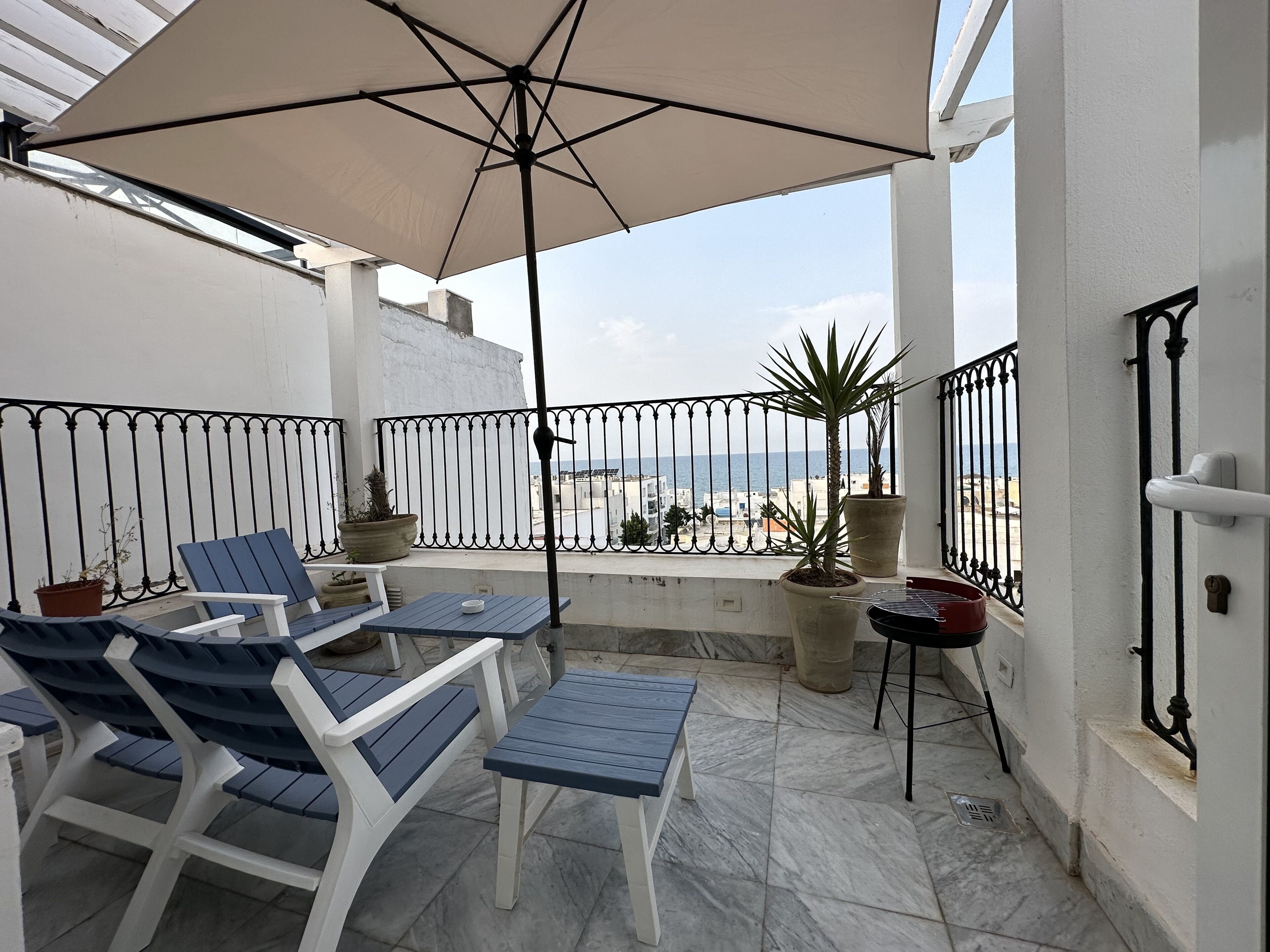 Un balcon avec une table et des chaises, des plantes en pot et une vue sur la mer.