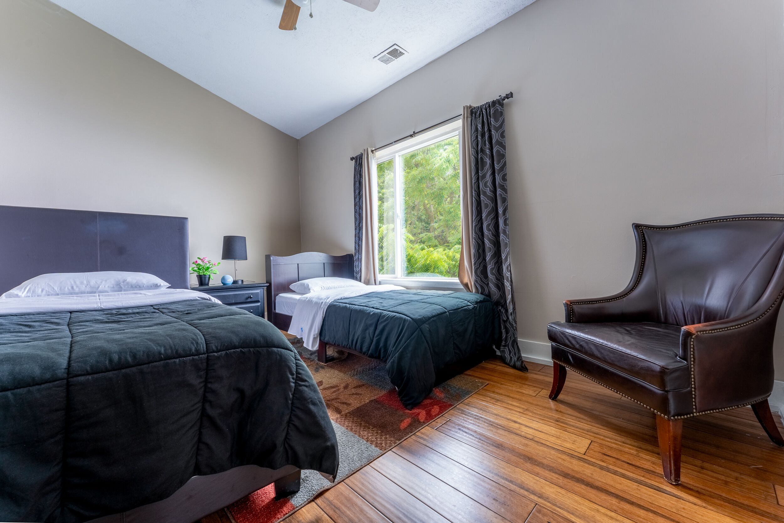 A bedroom with two beds, a chair, a nightstand, and a window with curtains.