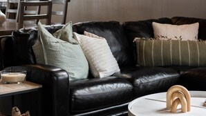 A modern living room with a black leather sofa, a round white coffee table, and three framed pictures on the wall. - Shanty Creek Escape l Ski l Hot Tub l Pool (Bellaire)