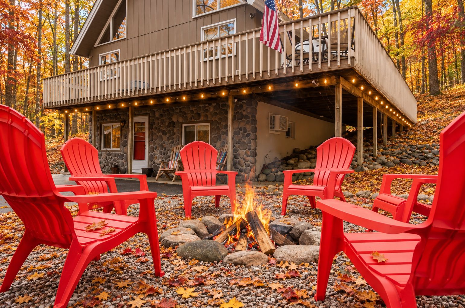 Een chalet met een stenen gevel, een terras met lichtjes en rode Adirondack-stoelen rond een vuurkuil.