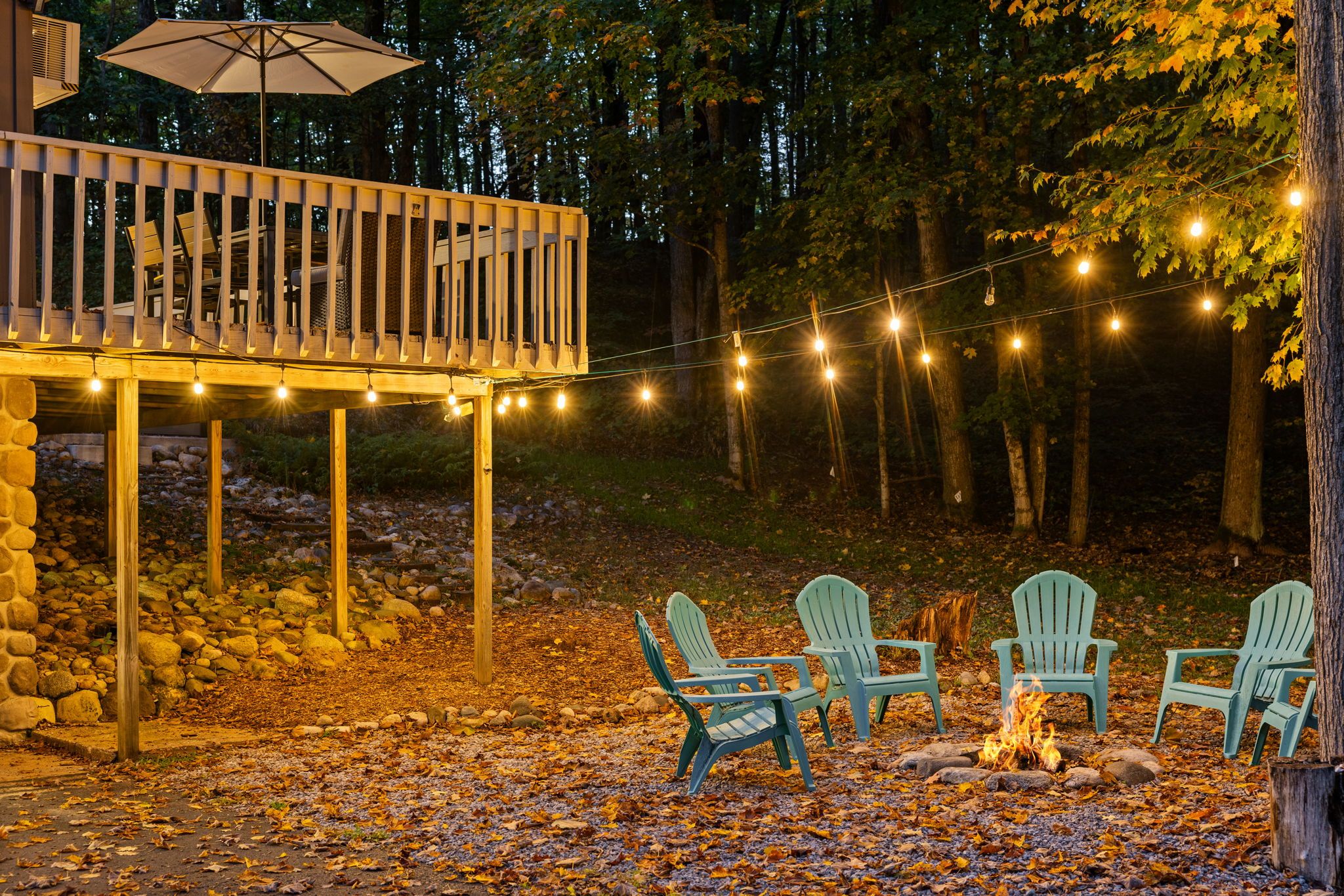 A wooden deck with string lights, outdoor seating, and a fire pit.
