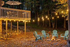 Une terrasse en bois agrémentée de guirlandes lumineuses, d’un espace salon extérieur et d’un foyer.