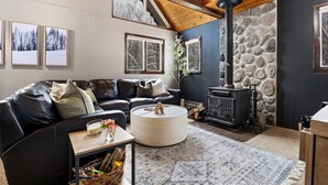 A cozy living room with a stone wall, a fireplace, a leather sofa, and framed pictures on the wall. - Shanty Creek Escape l Ski l Hot Tub l Pool (Bellaire)