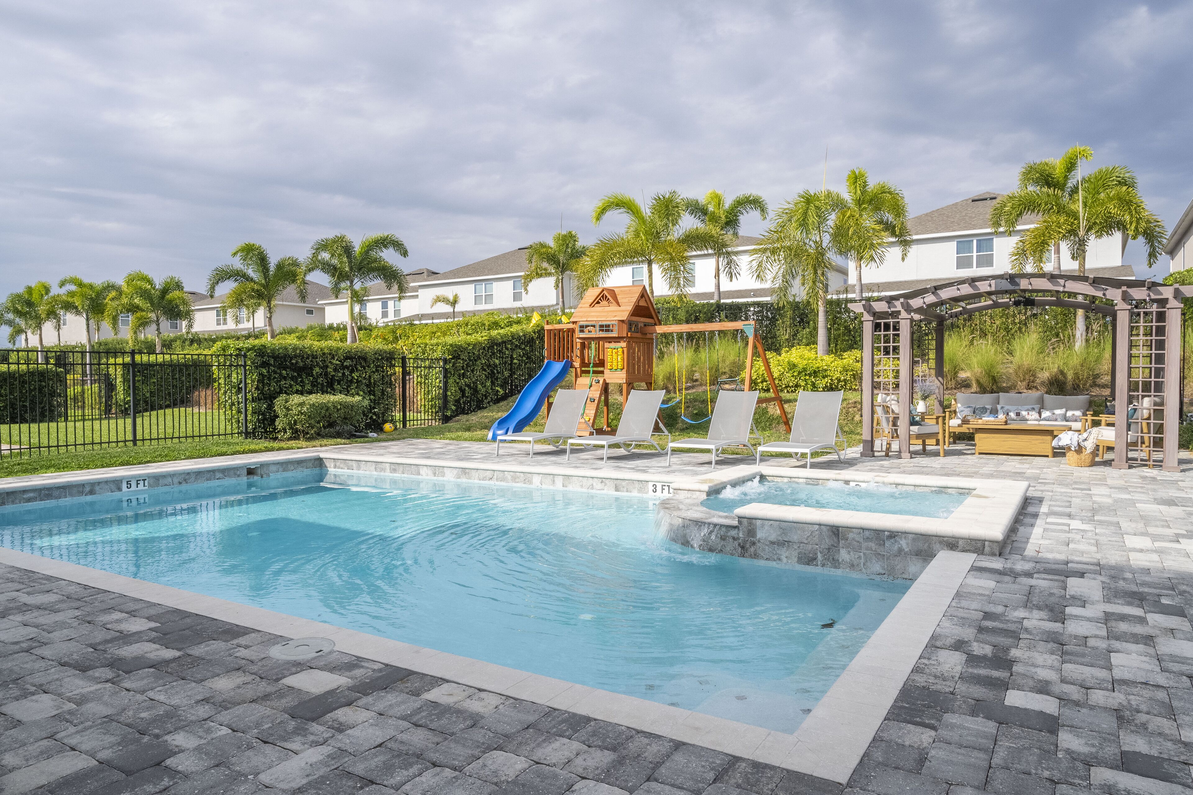 A swimming pool with a slide and lounge chairs, surrounded by palm trees and a gazebo.