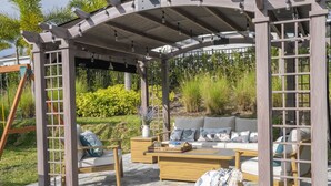 A covered outdoor seating area with a wooden pergola, cushioned seating, and a stone-tiled floor. - House Resort at Encore Reunion - Disney (Kissimmee)