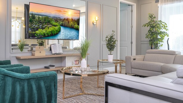 A modern living room with a flat-screen TV, green velvet chairs, a glass coffee table, and a beige sofa. - House Resort at Encore Reunion - Disney (Kissimmee)