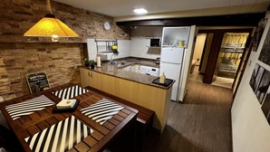 A compact kitchen with a dining area, featuring a stone wall, a wooden table with striped cushions, and a yellow pendant light. - Céntrico Apartamento en Lekeitio - Urrondo (Lekeitio)