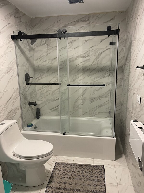 Een moderne badkamer met een douchecabine van glas, een wit toilet en een bad.
