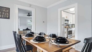 A dining area with a wooden table set for four, white walls, and a view into the kitchen.