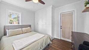 Ein Schlafzimmer mit Bett, Kleiderschrank, Deckenventilator und Fenster.