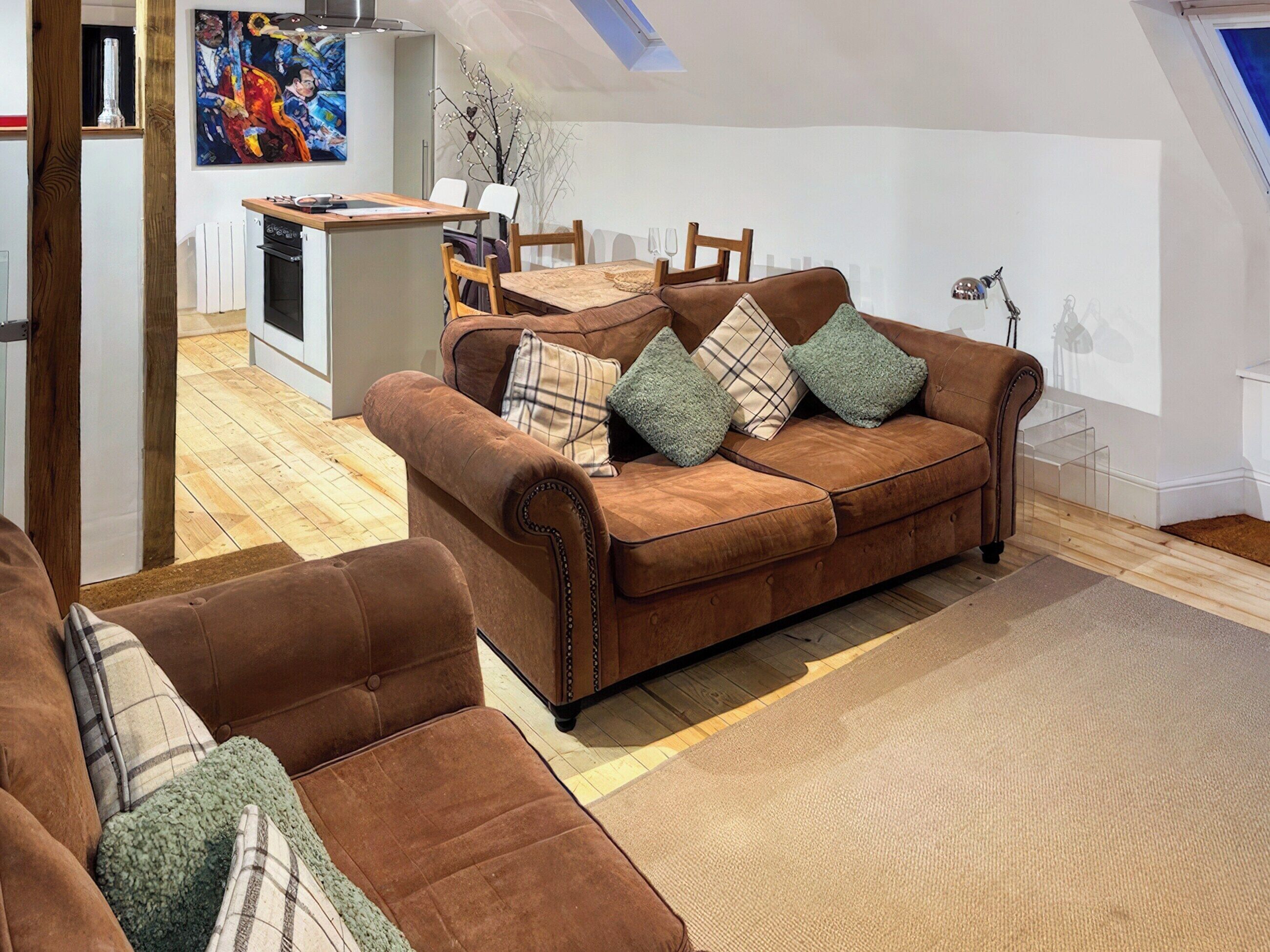 A cozy living room with a brown sofa set, a dining area with a table and chairs, and a kitchen in the background.