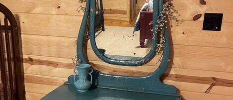 A blue dresser with a mirror and a small cup on top, against a wooden wall.
