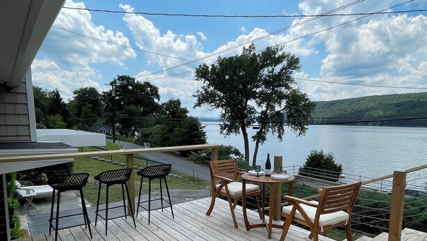 A wooden deck with outdoor seating, overlooking a lake and hills.