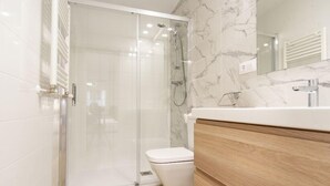 A modern bathroom with a glass shower enclosure, a white toilet, and a wooden vanity with a mirror. - VIZCAINOS GARDEN (Segovia)
