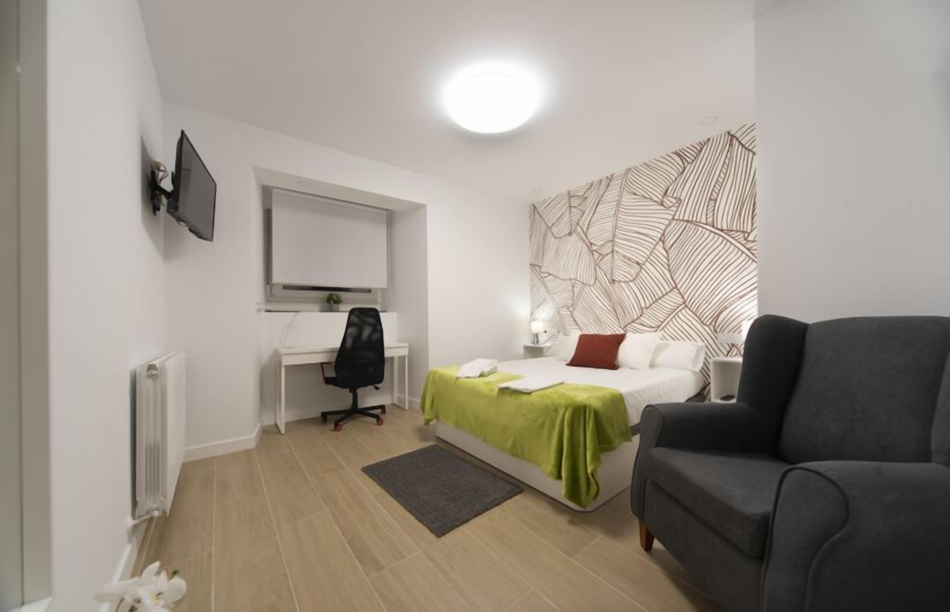 A modern bedroom with a bed, a desk, a chair, and a sofa.