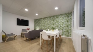 A modern living room with a dining table, grey sofa, and a flat-screen TV mounted on the wall. - VIZCAINOS GARDEN (Segovia)