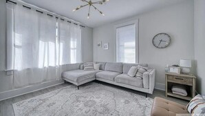 Uma sala de estar moderna com um sofá seccional, um tapete estampado, uma mesinha de madeira e um relógio de parede.