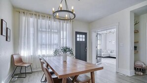 Uma área de refeições com mesa de madeira, cadeiras, um candelabro e vista para outro cômodo.