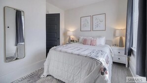 Um quarto com cama, mesas de cabeceira, espelho e quadros na parede.