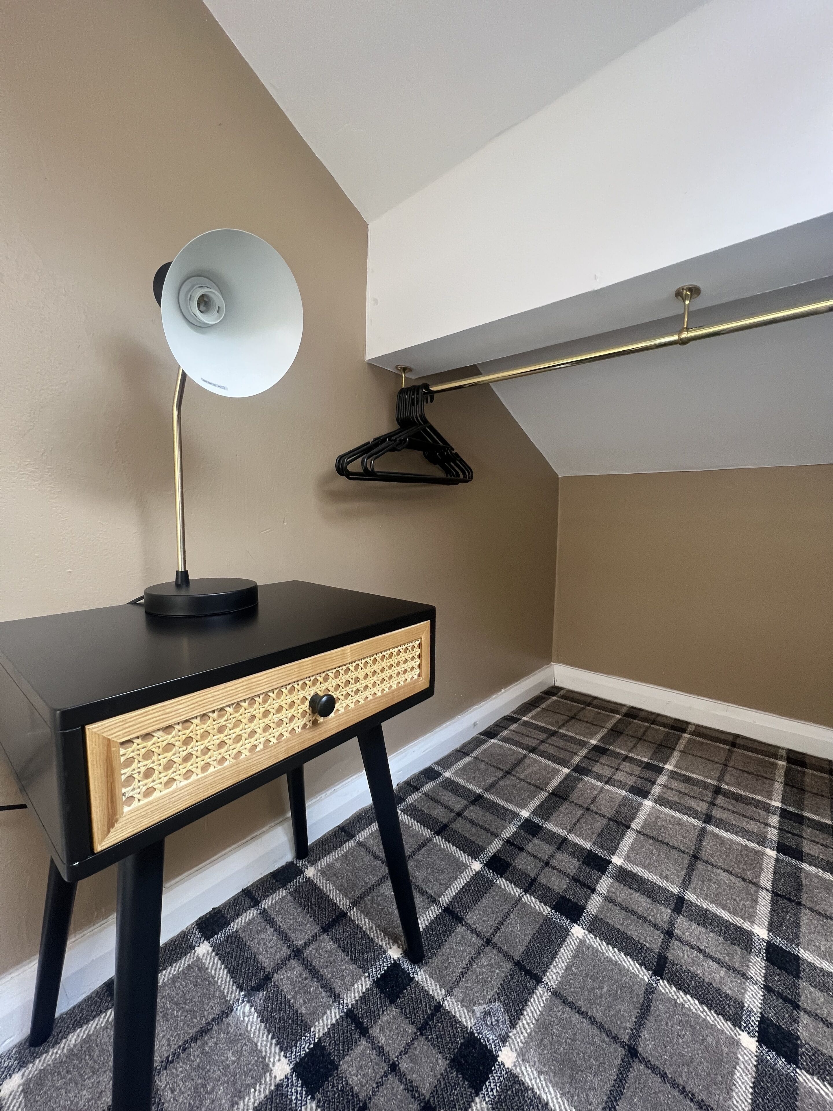 A room with a black desk, a white lamp, a black hanger, and a checkered carpet.