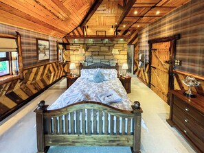 A wooden room with a bed, two nightstands, a stone wall, and wooden doors.
