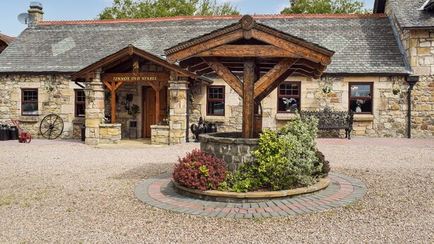 A stone building with a wooden porch and a sign reading 'Tennox Old Stable.' - Tennox Stables - UK39975 (Kilbirnie)