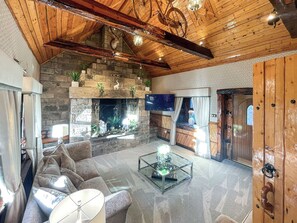 A spacious living area with a stone fireplace, a television mounted on the wall, and a wooden ceiling. - Tennox Stables - UK39975 (Kilbirnie)