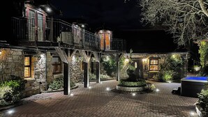 En innergård med en byggnad i sten, ett bubbelbad och ett väl upplyst utomhusområde på kvällen.
