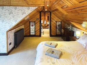 A bedroom with a sloped ceiling, a bed with two pillows, a nightstand with a lamp, and a dresser.