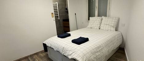 A bedroom with a bed, wooden flooring, a window, and a built-in wardrobe.